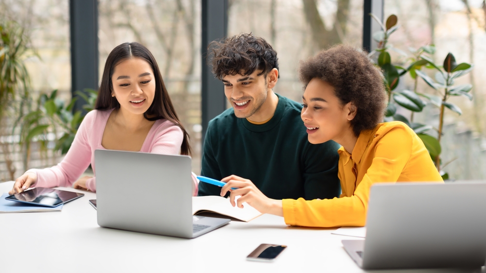 Happy,International,Students,Friends,Sitting,At,Desk,In,Coworking,Space